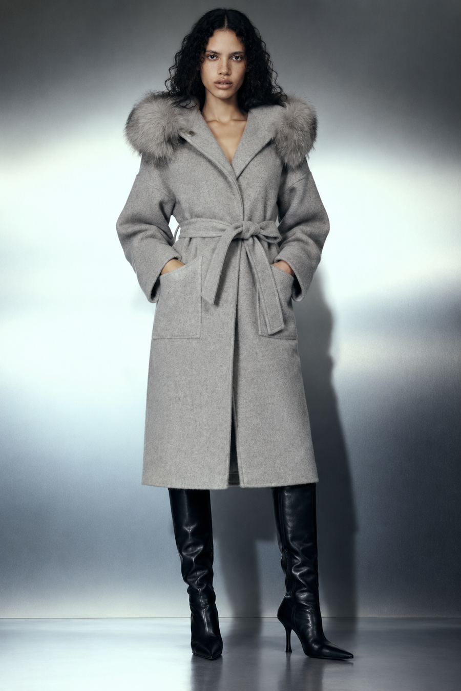 The Samara Long Coat — long manteau en laine grise à capuche bordée de fourrure de renard, porté plein pied de face